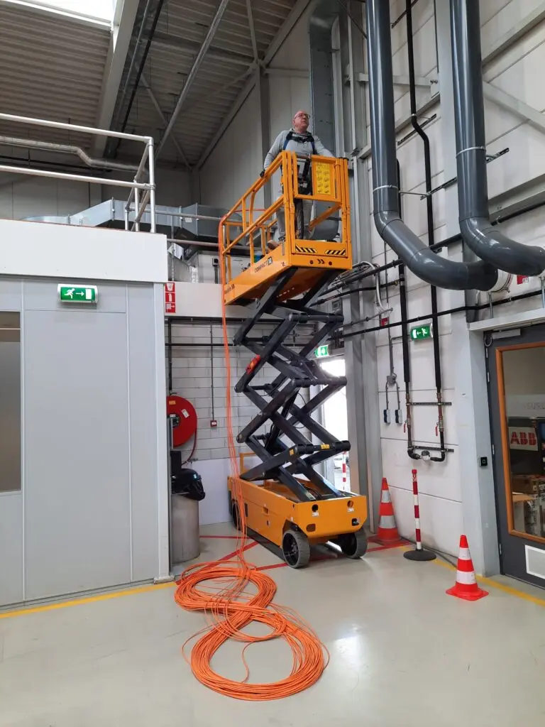 IT-technicus voert netwerkinstallatie uit met hoogwerker in industriële omgeving in Nederland